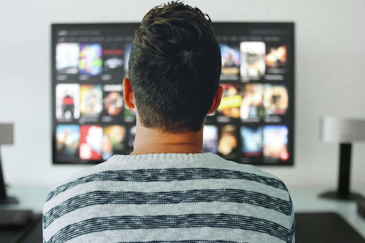 A man sits in front of a television, engrossed in a movie. Subtitles for the deaf and hard-of-hearing (SDH) are displayed on the screen.